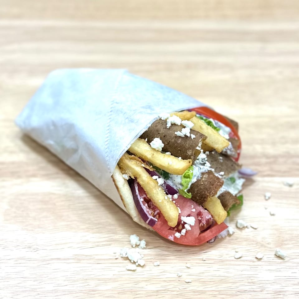 Mediterranean gyro with meat, fries, tomatoes, onions, and feta cheese, wrapped in paper.
