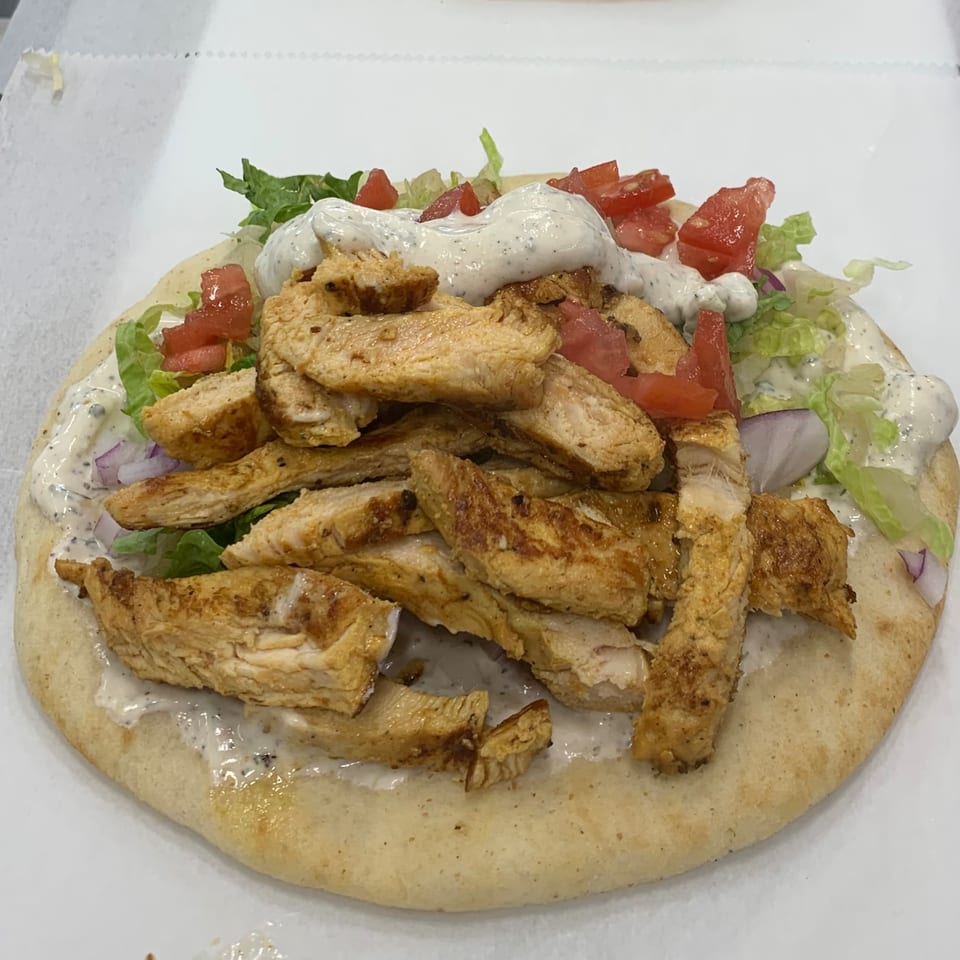 Mediterranean chicken gyro on pita bread with lettuce, tomatoes, onions, and white sauce.